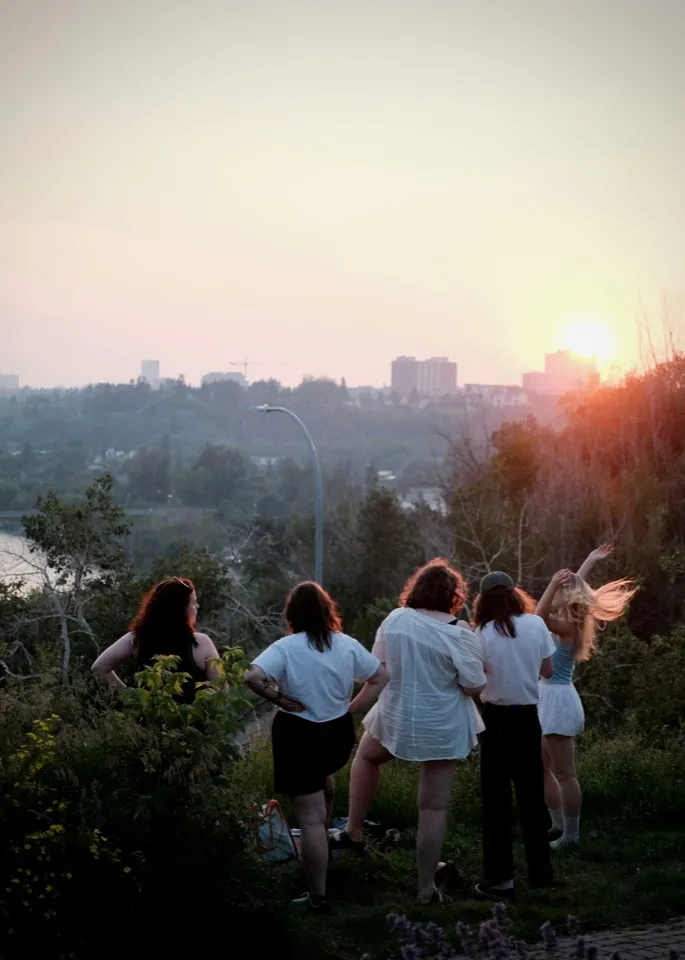 Un groupe de jeunes de dos face à la ville, au soir