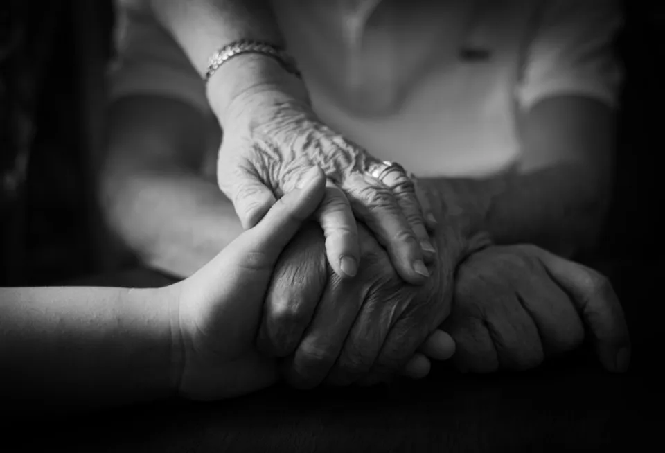 Une main d’enfant tenant une main très âgée, en noir et blanc